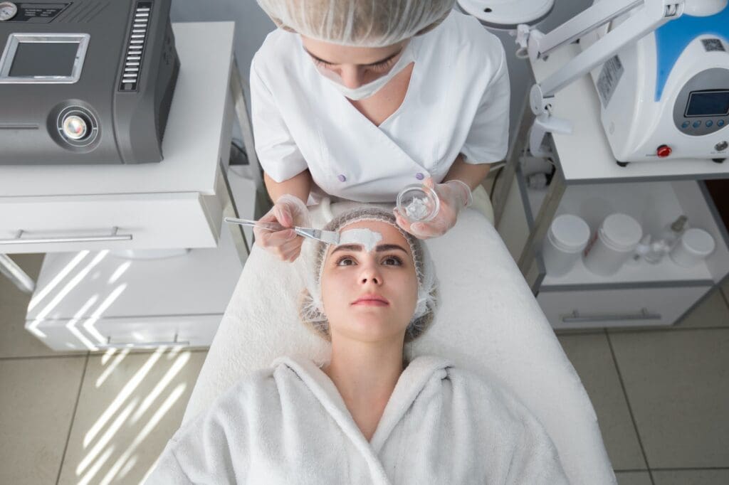 Woman applying facial mask treatment to patient