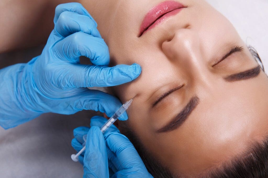 Closeup of blue medical gloves with syringe injecting fluid into face