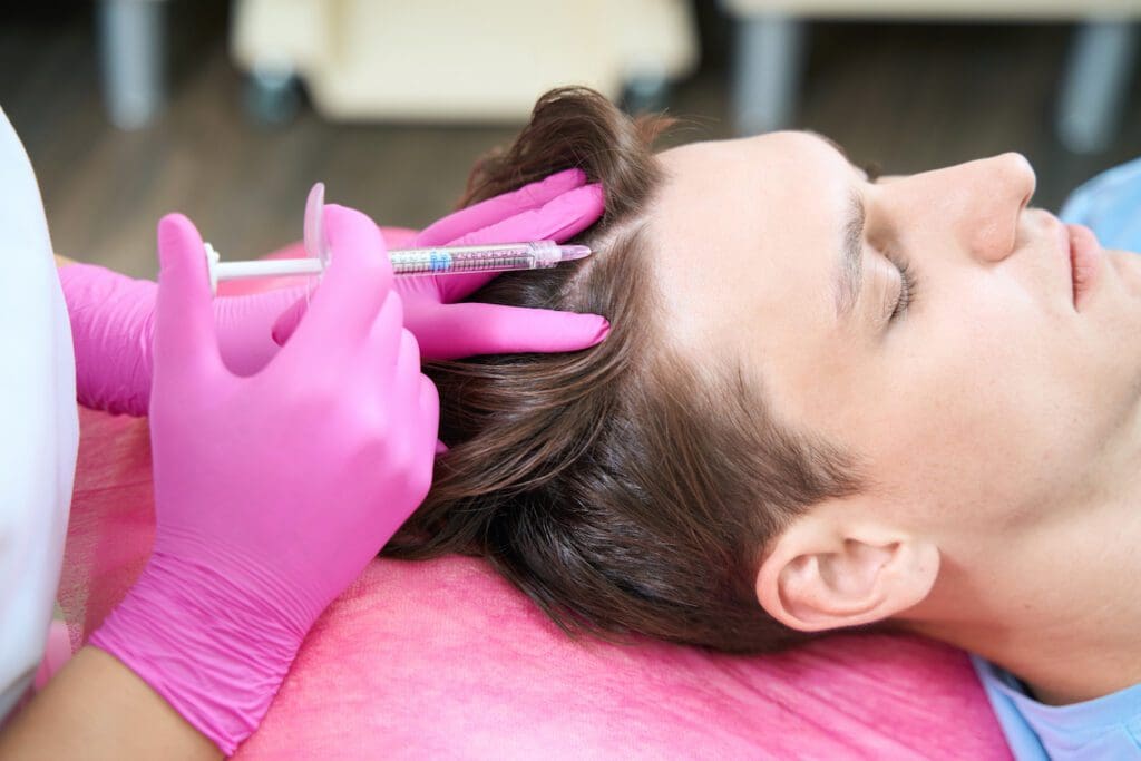 Close up of young man lying on couch in beauty clinic while doctor is doing mesotherapy for head